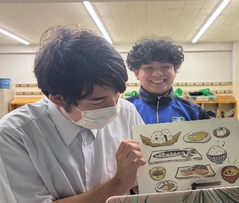 日本食の絵を手に説明する生徒と笑顔の生徒
