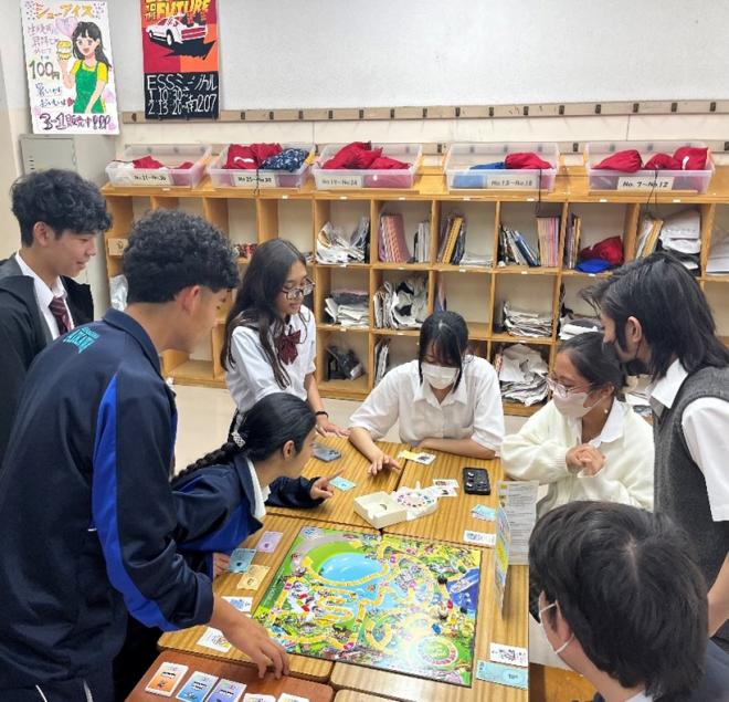 机上の人生ゲームを8人の生徒がのぞき込んでいる様子