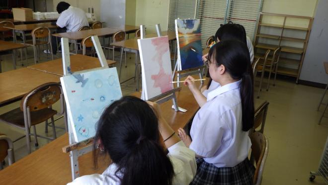 3人の美術部員がそれぞれの絵に色を塗っている様子