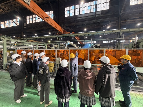 工場の中で作業機械の説明を受ける生徒たち