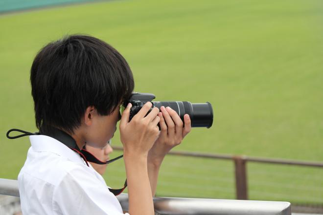 硬式野球部の試合を一眼レフで撮影する部員を撮影しました。